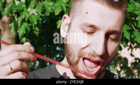 Er schlürft einen coolen Cocktail und macht eine Pause im Freien. Umgeben von lebhaftem Sommerlaub, genießt er den erfrischenden Geschmack des Sommers. Stockfoto