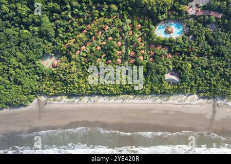 Hotelresort mit Swimmingpool auf Tennisplatz und Villendach neben der Strandküste, die über der Drone liegt Stockfoto