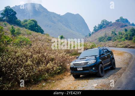 Ein Toyota Fortuner mit thailändischen Platten, der durch die malerische Landschaft von Laos fährt. Stockfoto