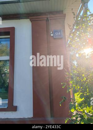 Nahaufnahme eines rot gerahmten Fensters an einer weißen Gebäudefassade, das die Reflexion der umgebenden Strukturen einfängt. Die klaren Linien und kräftigen Farben entsprechen Stockfoto