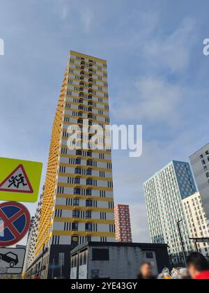 Zwei Hochhäuser, eines gelb-weiß, das andere grau, ragen über einem Parkplatz. Das klare, geometrische Design betont modernes urb Stockfoto