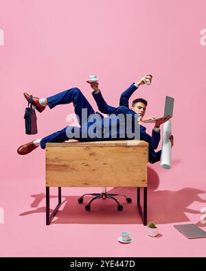 Konzeptuelle Collage. Junger Geschäftsmann in blauem Anzug balanciert auf dem Schreibtisch, während er mehrere Gegenstände, Kaffee, Laptop und Dokumente hält. Stockfoto