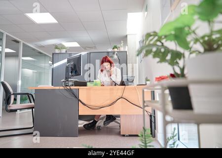 Vollständige Ansicht einer Sekretärin, die am Telefon an der Rezeption des Büros spricht. Lächelnde Geschäftsfrau, die Termine verwaltet. Stockfoto