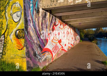 Graffiti und Schatten unter der Donnington Brücke über die Themse. Es ist früh an einem Herbstmorgen und ich bin auf meinem täglichen Spaziergang. Ich bin unter der Donnington Brücke über die Themse, direkt unterhalb von Oxford. Dies ist eine moderne Straßenbrücke, die die B4495 von der Abingdon Road zur Iffley Road führt. Er überquert den Fluss an der Grenze zwischen Iffley Lock und Osney Lock. Dies ist Teil des Thames Path Walkway, einer Strecke, die häufig von Radfahrern, Joggern und Hundebesitzern besucht wird - ganz zu schweigen von Fotografen! Hier sehen wir, wie mein Schatten die Brücke inspiziert. Stockfoto