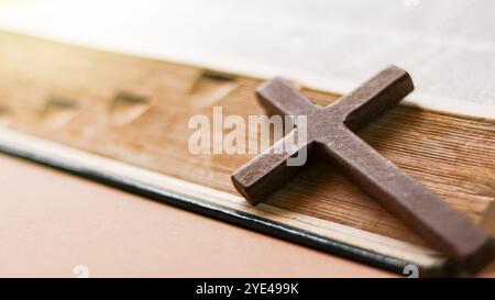 Dunkelrotes Holzkreuz, das sich an ein altes offenes Buch lehnt, das die Verbreitung der Liebe Jesu Christi unter Christen symbolisiert, die den Glauben und die Hingabe widerspiegelt Stockfoto