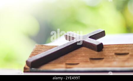 Dunkelrotes Holzkreuz, das sich an ein altes offenes Buch lehnt, das die Verbreitung der Liebe Jesu Christi unter Christen symbolisiert, die den Glauben und die Hingabe widerspiegelt Stockfoto