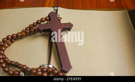 Dunkelrotes Holzkreuz, das sich an ein altes offenes Buch lehnt, das die Verbreitung der Liebe Jesu Christi unter Christen symbolisiert, die den Glauben und die Hingabe widerspiegelt Stockfoto