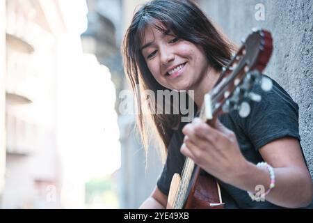Porträt einer brünetthaarigen Latina-Frau, die Gitarre spielt. Seitenansicht einer hübschen Frau, die lächelt. Stockfoto