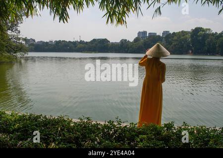 Hanoi, Vietnam: Vietnamesische Frau, die vor der Sonne mit ihrem traditionellen konischen Hut von Non La schützt, vor dem Hoan Kiem See (Schwertsee), Altstadt Stockfoto