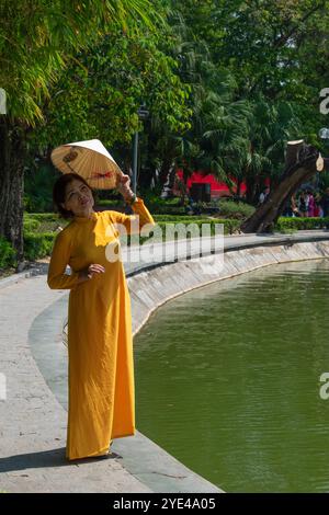 Hanoi, Vietnam: Vietnamesische Frau, die vor der Sonne mit ihrem traditionellen konischen Hut von Non La schützt, vor dem Hoan Kiem See (Schwertsee), Altstadt Stockfoto