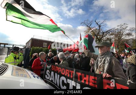 Shenstone, England, Großbritannien. Oktober 2024. Demonstranten halten ein Banner, um den Fortschritt eines Polizeifahrzeugs zu verhindern, während ein anderer während der Demonstration eine palästinensische Flagge vor UAV-Motoren schwingt. Pro-palästinensische Demonstranten halten Druck auf die israelische Rüstungsfirma Elbit Systems in ihrer UAV-Triebwerksanlage in Shenstone. Sie fordern weiterhin, dass das Unternehmen keine Teile für Drohnen mehr produziert, die verheerend gegen das palästinensische Volk in Gaza, die Libanesen und die Bevölkerung im Nahen Osten eingesetzt werden. Demonstranten, einschließlich Unterstützern der pro-palästinensischen Gruppe Palestine Action, werden entsandt Stockfoto