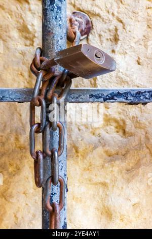 Rostige Kette und Vorhängeschloss auf Eisenzaun gegen Wand Stockfoto