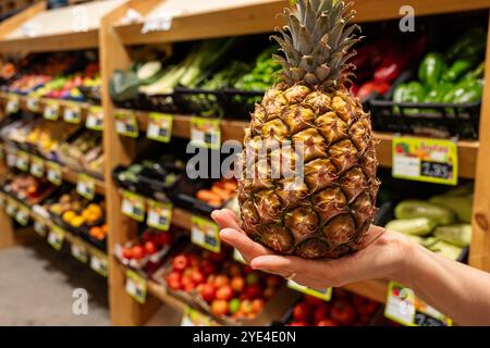 Eine Person hält eine Ananas in einem Supermarkt. Das Geschäft ist mit frischen Produkten gefüllt, darunter eine Vielzahl von Obst und Gemüse Stockfoto