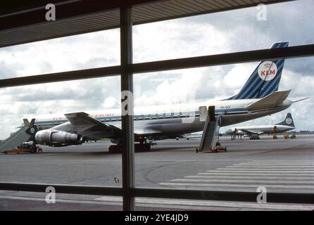 Amsterdam, Niederlande. August 1961: Blick auf ein Douglas DC-8-53-Flugzeug der KLM (Royal Dutch Airlines), das auf dem Vorfeld des Flughafens Schiphol in Amsterdam geparkt ist. Das Foto, das von einer Witwe aus einem Terminalgebäude aufgenommen wurde, zeigt, wie das Flugzeug für den Flug vorbereitet wird. Dieses Flugzeug wurde im Mai 1961 an KLM geliefert, nur drei Monate vor diesem Foto, und es ist in seiner ursprünglichen Lackierung zu sehen. Sie blieb bis 1976 bei der Fluggesellschaft im Dienst. Sichtbar in der Entfernung ist ein KLM Convair CV-340 Flugzeug. Stockfoto