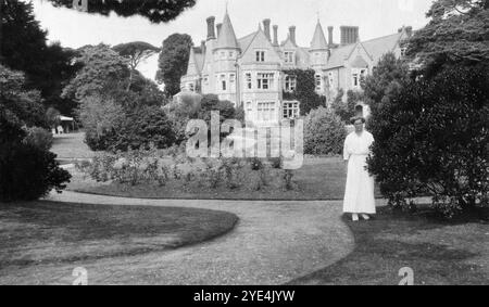 West Sussex, England. 1913 – Eine Frau, die vermutlich eine Verwandte der Familie Henty ist, posiert für ein Foto in den Gärten vor Ferring Grange in Ferring, einem Küstendorf in West Sussex. Das Anwesen war das Zuhause von Edwin Henty, J. P, D.L., F.S.A. (1844–1916), der als High Sheriff of Sussex gedient hatte. 1924 wurde das Haus in ein modisches Hotel umgewandelt, das von vielen Prominenten besucht wurde, darunter Edward, dem Prinzen von Wales (später bekannt als Duke of Windsor). Das Haus wurde im Oktober 1946 durch einen Brand zerstört. Stockfoto