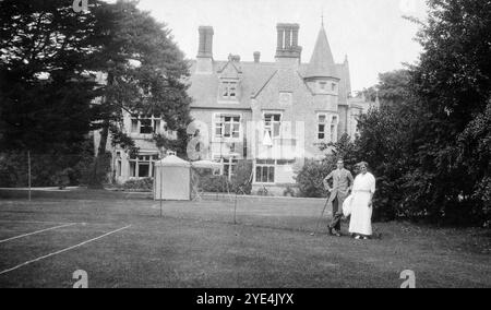 West Sussex, England. 1913 – Ein junger Mann und eine Frau, die vermutlich Verwandte der Familie Henty sind, posieren für ein Foto auf dem Tennisplatz auf dem Gelände von Ferring Grange in Ferring, einem Küstendorf in West Sussex. Der Mann hält einen Golfschläger. Das Anwesen war das Zuhause von Edwin Henty, J. P, D.L., F.S.A. (1844–1916), der als High Sheriff of Sussex gedient hatte. 1924 wurde das Haus in ein modisches Hotel umgewandelt, das von vielen Prominenten besucht wurde, darunter Edward, dem Prinzen von Wales. Das Haus wurde im Oktober 1946 durch einen Brand zerstört. Stockfoto