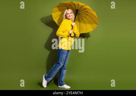 Foto der entzückenden netten Dame tragen trendige gelbe Kleidung halten Sonnenschirm isoliert auf grünem Hintergrund Stockfoto