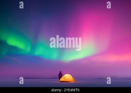 Touristen nahe gelbem Zelt im Winterfeld vor dem Hintergrund des unglaublichen Sternenhimmels mit Aurora Borealis. Wunderschöne Nachtlandschaft mit Polarlichtern. Nordlichter Stockfoto