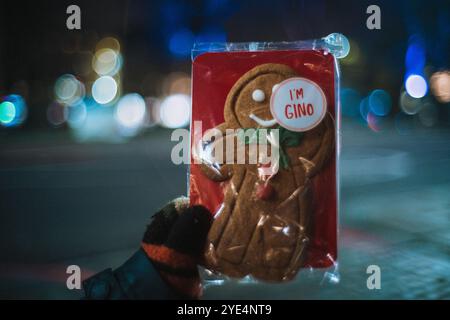 Kinderhand in einem gemütlichen Fäustling, der einen Lebkuchenkeks in der Form eines Mannes vor glühenden Weihnachtslichtern in der Nacht hält. Stockfoto