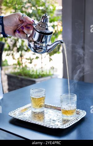 Marrakesch Marokko Ein Tourist gießt einen frisch gebrühten Pfefferminztee in ein Glas aus einer silbernen Teekanne. Der Tee ist ein erfrischendes traditionelles marokkanisches Getränk Stockfoto