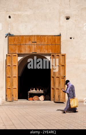 Marrakesch Marokko. Eine Frau läuft an einer handwerklichen Töpferei in der Medina vorbei, die Töpferschalen und Geschirr verkauft, die im Ladeneingang ausgestellt werden Stockfoto