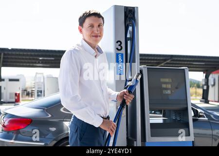 Der Mann hält eine Wasserstoffdüse an einer Wasserstofftankstelle. Auto mit Wasserstoff betanken. Stockfoto