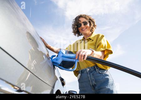 Die Frau hält eine Wasserstoff-Tankdüse. Betanken des Autos mit Wasserstoffkraftstoff. Stockfoto