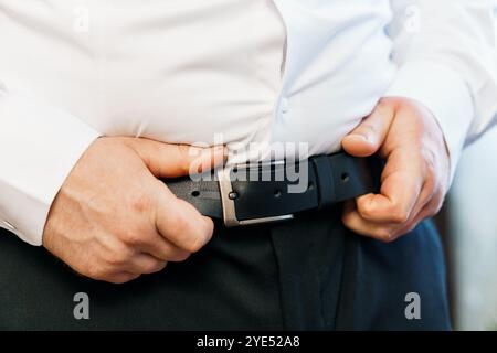 Mann, der seinen Gürtel anpasst, während er ein weißes Hemd trägt. Stockfoto