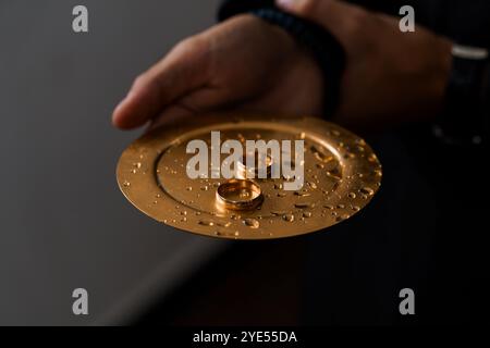 Reflektierende Momente: Hochzeitsringe auf einer Goldplatte mit Wassertropfen. Stockfoto