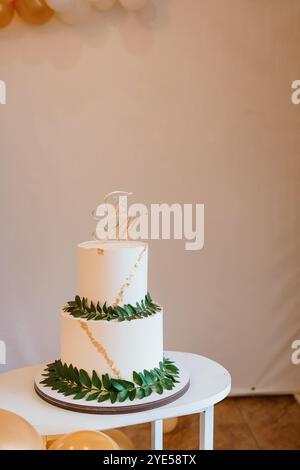 Eleganter dreistöckiger Hochzeitstorte mit goldenen Akzenten und grüner Dekoration. Stockfoto