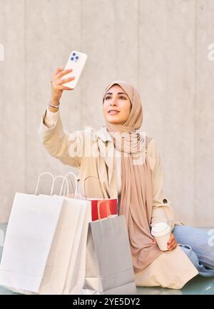 Frau macht ein Selfie mit ihrem Handy, während sie einen Kaffee trinkt, während sie eine Pause vom Einkaufen im Haushalt macht Stockfoto