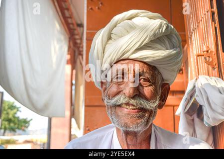 Älterer Mann mit traditionellem Rajasthani Turban lächelnd glücklich in die Kamera mit warmen Orangetönen im Hintergrund Stockfoto