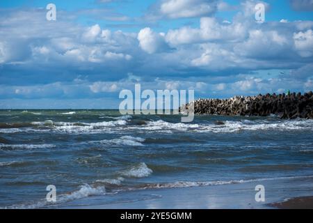 Die Sonne scheint auf ruhigem Wasser, während die Wellen sanft auf das Ufer Rollen, mit einem felsigen Steg, der sich bis in die Ferne unter einem Himmel voller Fluf erstreckt Stockfoto