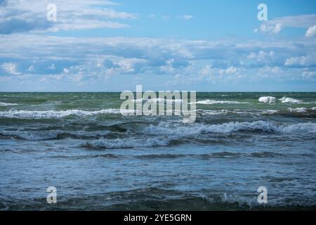 Sanfte Wellen Rollen auf die Sandküste und erzeugen ein beruhigendes Geräusch in einer ruhigen Küstenumgebung unter einem teilweise bewölkten Mittagshimmel. Stockfoto