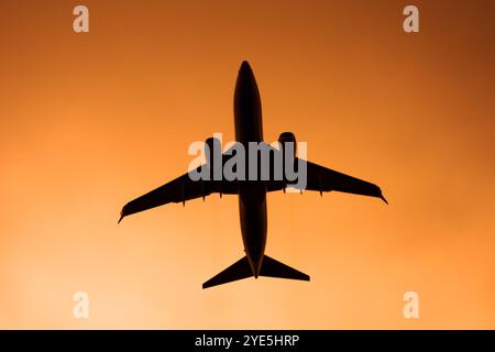 Jet Passagierflugzeug fliegt am orangefarbenen und gelben Sonnenuntergangshimmel, Blick von unten Stockfoto