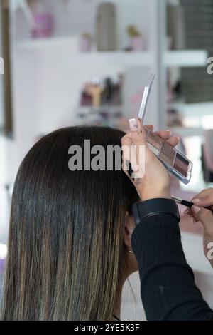 Eine Stylistin schminkt das Haar einer Frau. Der Stylistin verwendet einen Pinsel, um ein Produkt auf das Haar der Frau aufzutragen Stockfoto