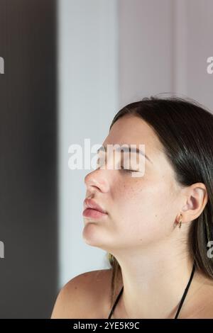 Eine Frau mit langen dunklen Haaren sitzt mit geschlossenen Augen. Sie trägt Ohrringe und eine Halskette Stockfoto