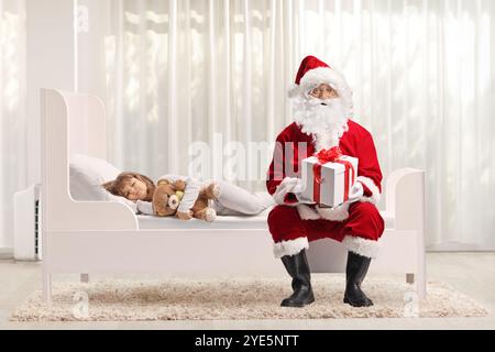 Ein Mädchen schläft im Bett und der weihnachtsmann hält eine Geschenkbox Stockfoto