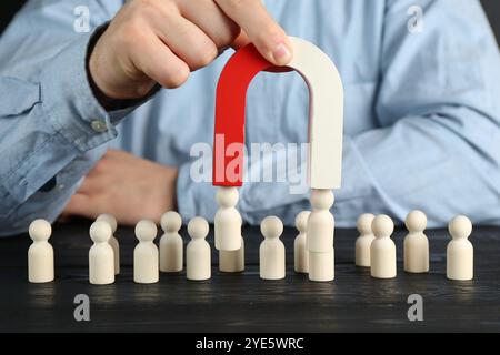 Mann mit Magnet, der menschliche Figuren an einem schwarzen Holztisch anzieht, Nahaufnahme Stockfoto