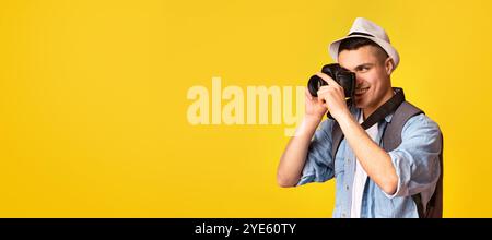 Aktiver glücklicher Reisender, der Fotos mit der Kamera über orangefarbenem Hintergrund macht Stockfoto