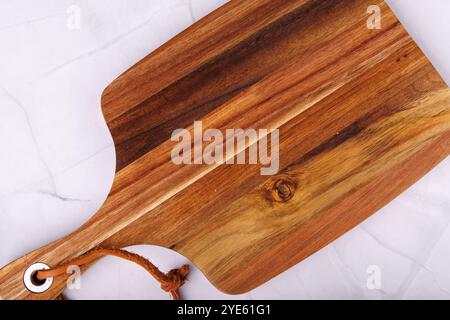 Ein Blick von oben auf ein hölzernes Schneidebrett, das auf einem klaren Marmortisch sitzt und sich auf die handwerklichen und natürlichen Elemente der Materialien konzentriert Stockfoto