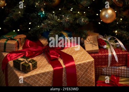 Nahaufnahme Hintergrundbild einer großen Geschenkbox mit roter Schleife, die unter dem Weihnachtsbaum in schwacher Beleuchtung gestapelt ist Stockfoto