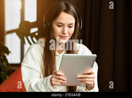 Modernes Mädchen mit Tablet und Kopfhörer arbeitet im Sessel Stockfoto