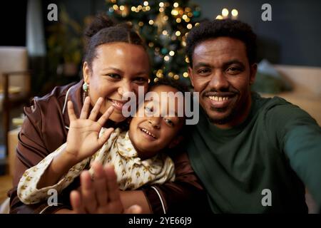 Vorderansicht Porträt der Familie Happy Black mit einem kleinen Jungen, der in der Kamera winkt und lächelnd mit Freunden und Familie im Video-Chat an Weihnachten spricht Stockfoto