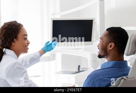 Afrikanische Zahnärztin zeigt auf leere Anzeige, zeigt Patienten etwas Stockfoto