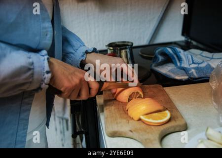 Eine Person schneidet gekonnt frische Zitrusfrüchte, einschließlich Orangen, auf einem Holzbrett. Die Küche hat eine warme Atmosphäre, gefüllt mit Morgenlicht Stockfoto