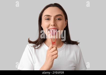 Junge Frau benutzt Zungenschaber auf hellem Hintergrund, Nahaufnahme Stockfoto