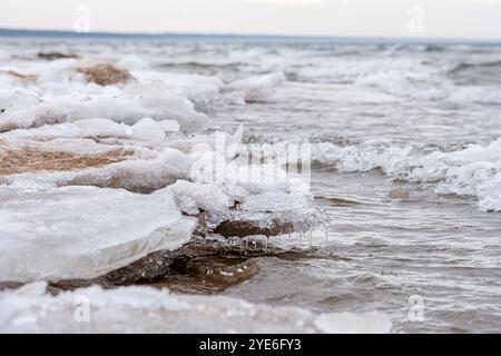 Der frühe Frühling schmilzt das Wintereis entlang des Seeufers und offenbart eine Mischung aus gefrorenem und fließendem Wasser. Sanfte Wellen Stockfoto