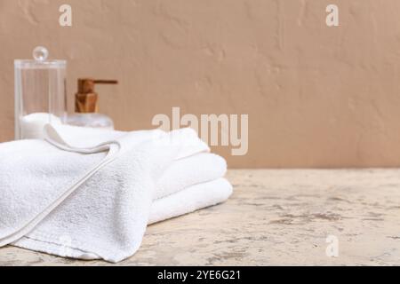 Reinigen Sie weiche Handtücher, eine Flasche Kosmetikprodukt und einen Halter mit Wattepads in der Nähe der braunen Wand, Nahaufnahme Stockfoto