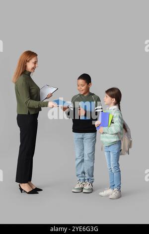 Reifer Lehrer gibt kleinen Schülern Werbetexte auf hellem Hintergrund Stockfoto